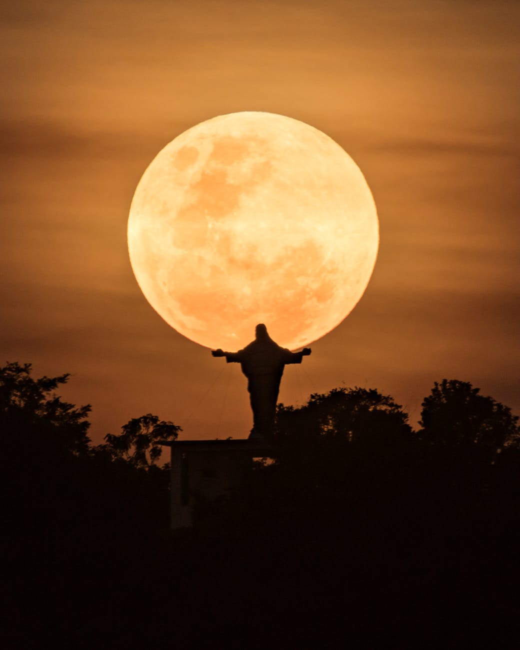 silhouette of man standing on top of building under full moon